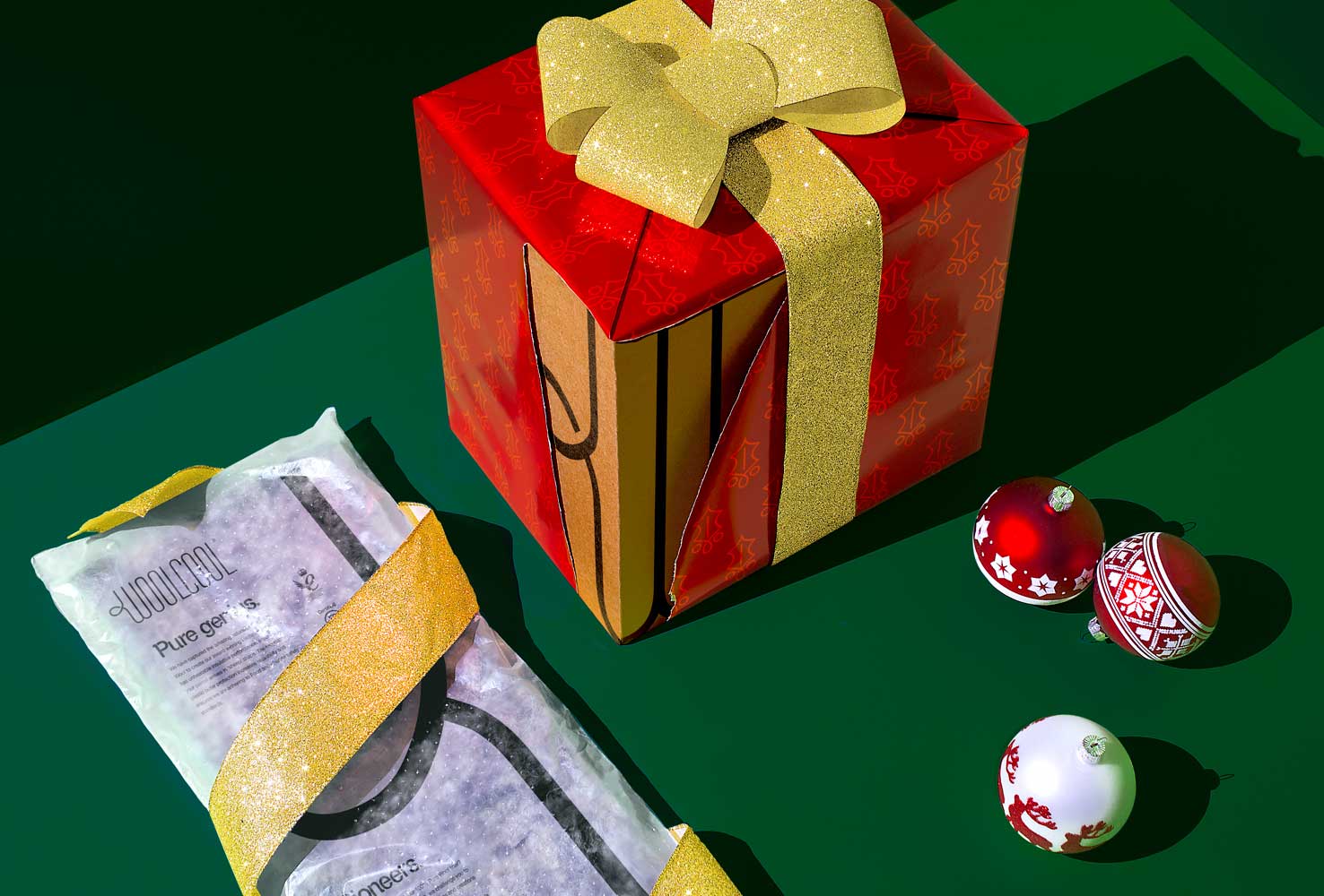 A Woolcool box and liner wrapped in Christmas paper on a green background with some baubles
