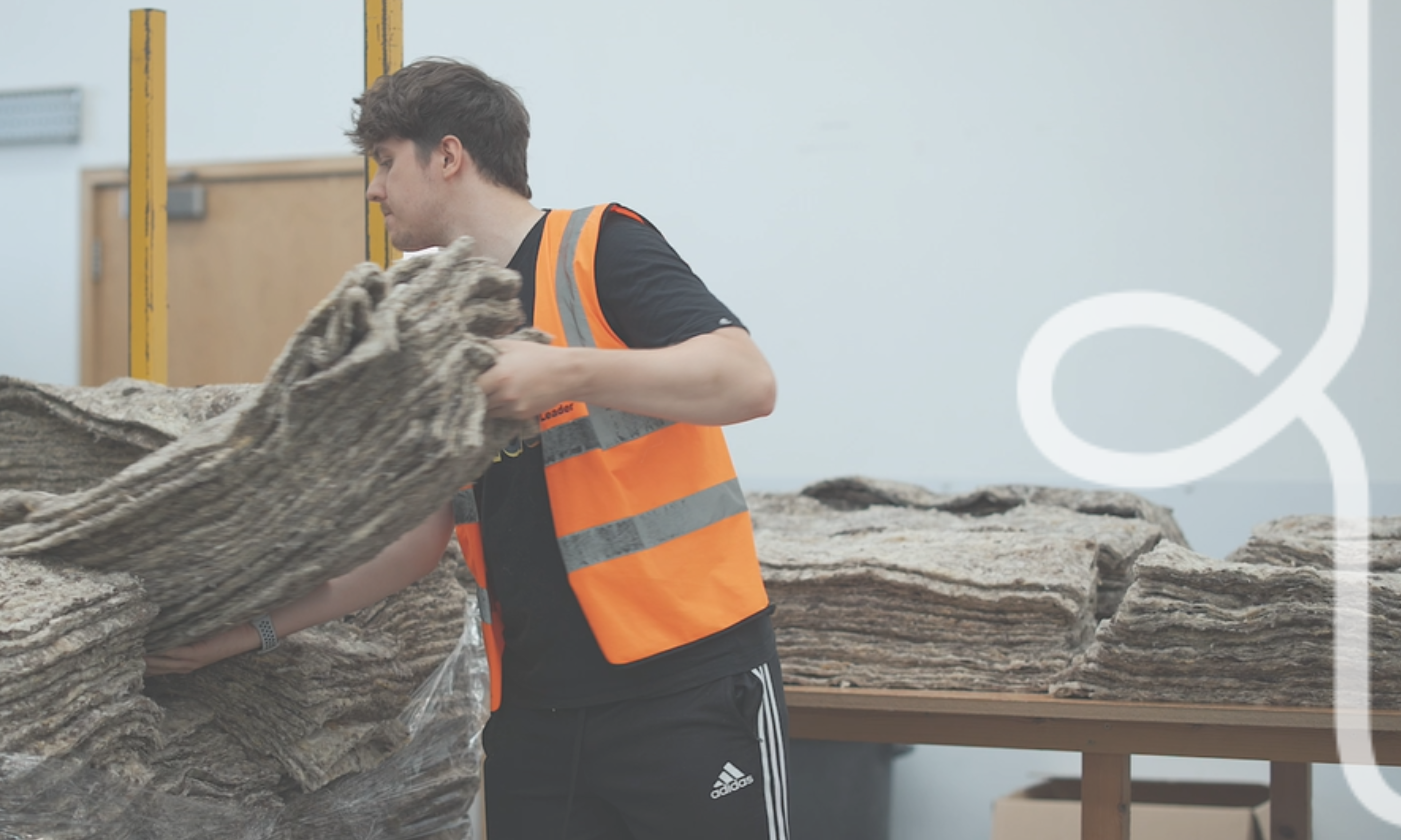 a warehouse operative, wearing an orange hi-vis jacket carrying a stack of felted wool fleece liners